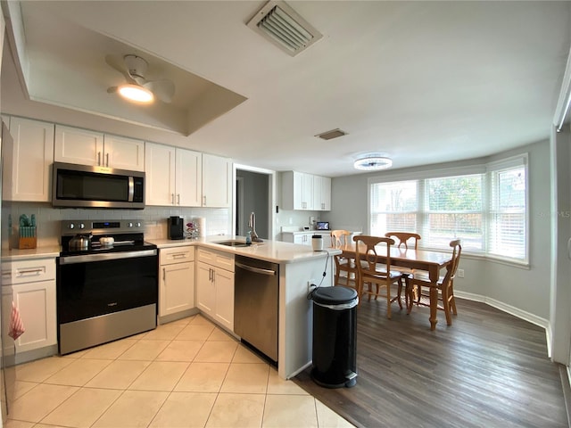 kitchen with sink, white cabinetry, a tray ceiling, kitchen peninsula, and stainless steel appliances