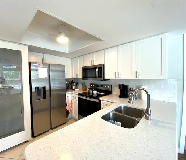 kitchen featuring white cabinetry, sink, decorative backsplash, a tray ceiling, and stainless steel appliances