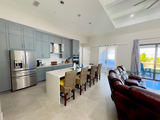 kitchen featuring stainless steel fridge with ice dispenser, visible vents, backsplash, wall chimney range hood, and a kitchen breakfast bar