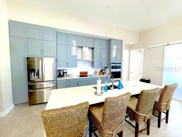 kitchen featuring blue cabinets, a sink, a kitchen breakfast bar, appliances with stainless steel finishes, and wall chimney exhaust hood