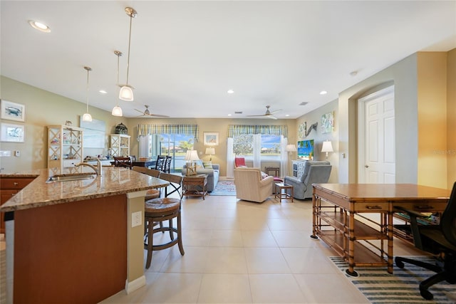 kitchen featuring light tile patterned flooring, sink, hanging light fixtures, ceiling fan, and light stone countertops