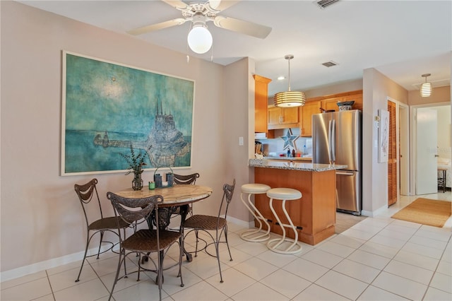 kitchen with light tile patterned flooring, stainless steel fridge, hanging light fixtures, light stone counters, and kitchen peninsula