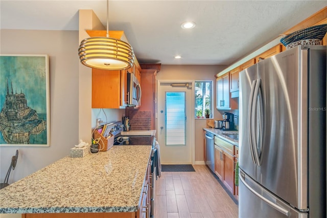 kitchen with pendant lighting, stainless steel appliances, light stone countertops, and light hardwood / wood-style floors