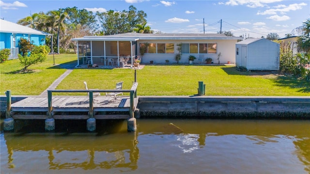 back of property with a lawn, a storage unit, and a water view