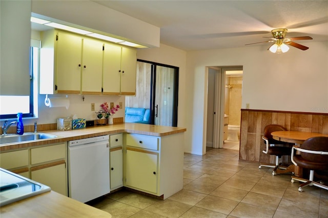 kitchen with light countertops, wainscoting, a sink, dishwasher, and a peninsula