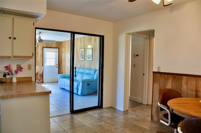 doorway to outside with wainscoting, light tile patterned flooring, ceiling fan, and wood walls