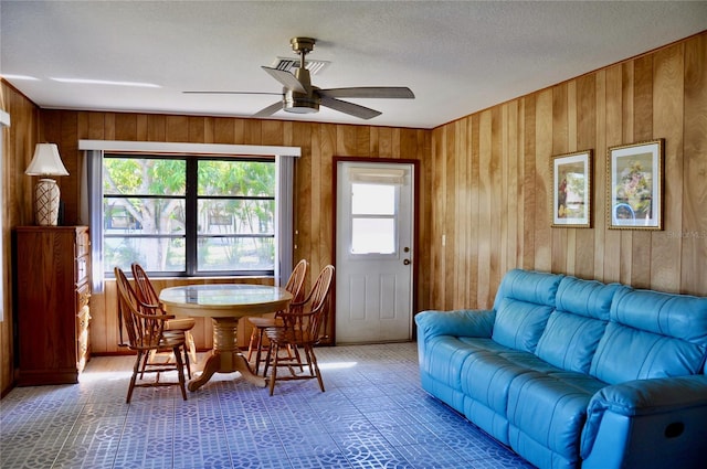 dining space featuring wood walls, a textured ceiling, visible vents, and a ceiling fan