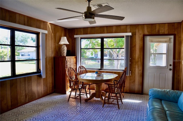 dining room with a healthy amount of sunlight, wood walls, and a ceiling fan