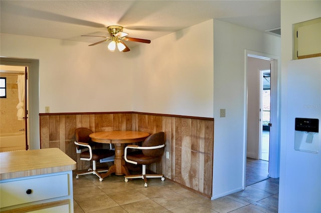 dining space featuring ceiling fan, wainscoting, light tile patterned flooring, and wooden walls