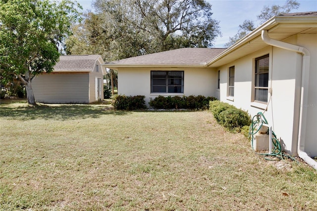 exterior space with stucco siding, a front yard, a storage unit, and an outbuilding