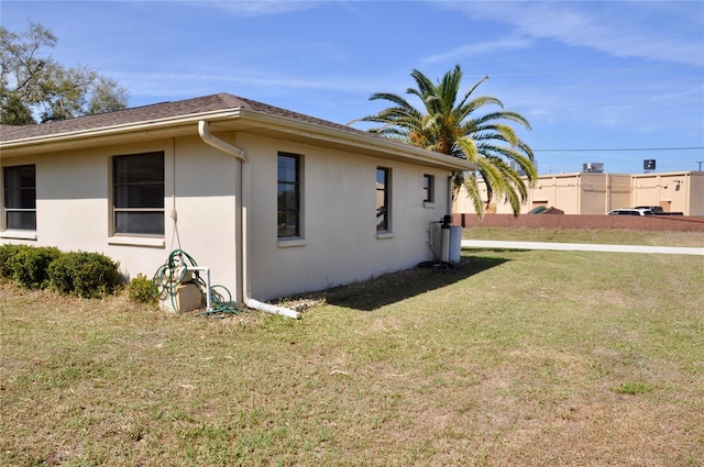 view of side of property featuring a shingled roof, a yard, and stucco siding