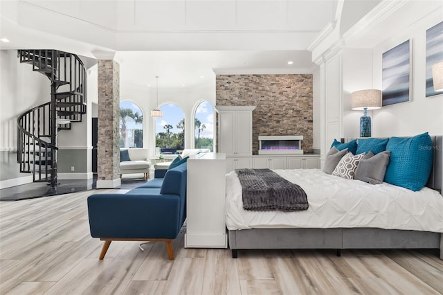 bedroom featuring light hardwood / wood-style floors, decorative columns, a fireplace, and a towering ceiling