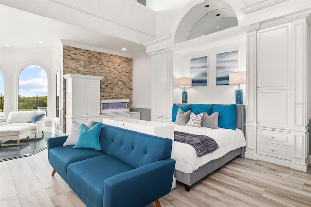 bedroom featuring ornamental molding, light wood-type flooring, and a towering ceiling