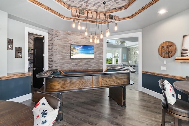 recreation room with a raised ceiling, brick wall, and dark hardwood / wood-style floors