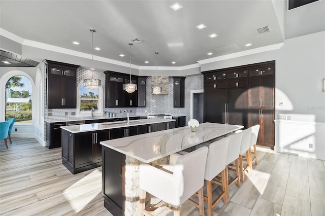 kitchen featuring dark brown cabinetry, pendant lighting, backsplash, sink, and a kitchen island with sink