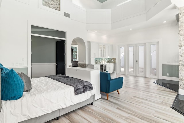 bedroom featuring light wood-type flooring, french doors, access to outside, wine cooler, and a high ceiling