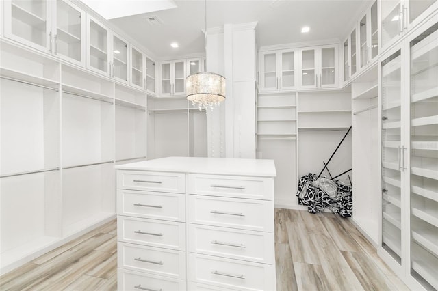 spacious closet with light hardwood / wood-style flooring and a chandelier