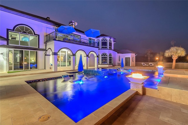 pool at night with a patio and a hot tub