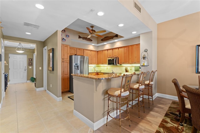 kitchen featuring visible vents, appliances with stainless steel finishes, a breakfast bar, and light stone counters