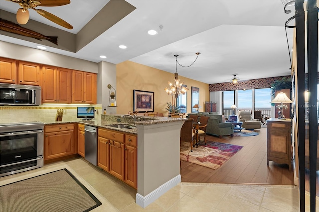 kitchen featuring light stone counters, stainless steel appliances, a peninsula, a sink, and brown cabinetry