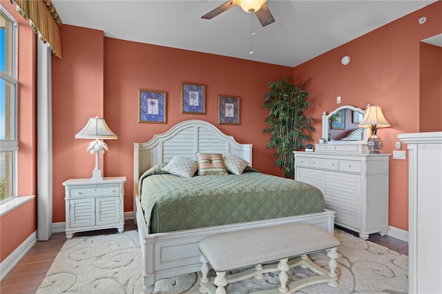 bedroom with light wood-style floors, an accent wall, baseboards, and a ceiling fan