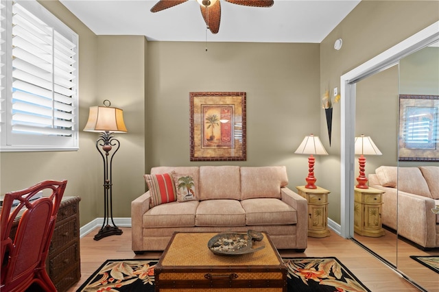 living area with baseboards, ceiling fan, and light wood finished floors