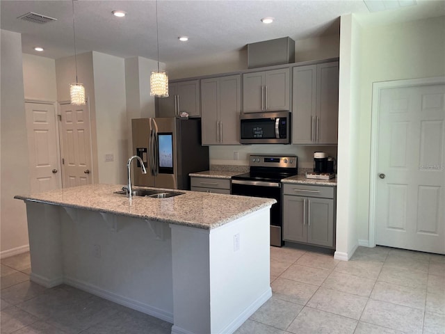 kitchen with appliances with stainless steel finishes, light stone counters, an island with sink, pendant lighting, and sink