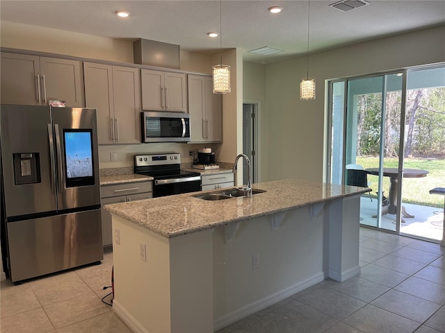 kitchen with sink, gray cabinets, light stone counters, appliances with stainless steel finishes, and a kitchen breakfast bar