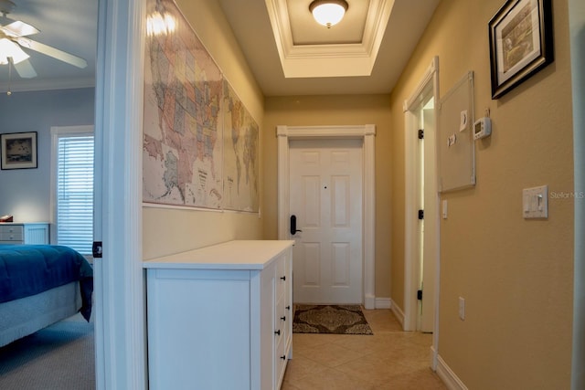 hall with light tile patterned flooring, ornamental molding, and a raised ceiling