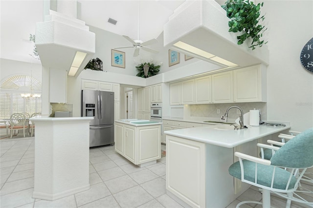 kitchen featuring sink, stainless steel fridge, a towering ceiling, a center island, and kitchen peninsula