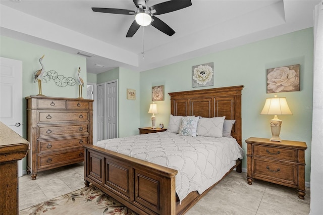 bedroom with light tile patterned floors, visible vents, ceiling fan, a closet, and a raised ceiling