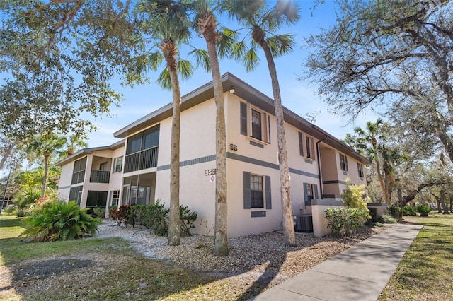 view of side of property with a yard, cooling unit, a balcony, and stucco siding