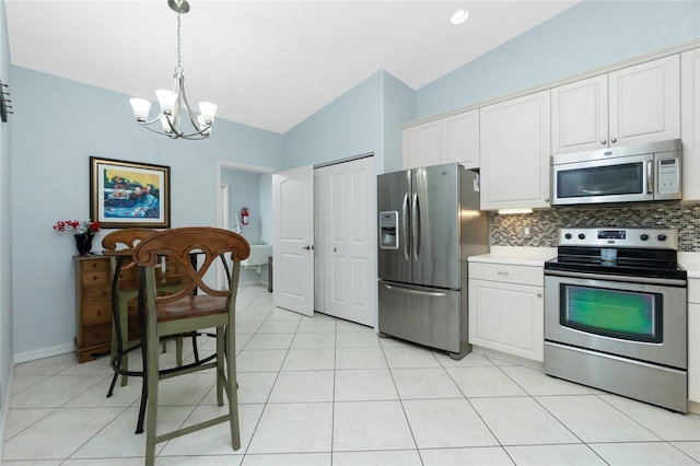 kitchen with appliances with stainless steel finishes, vaulted ceiling, white cabinetry, hanging light fixtures, and decorative backsplash