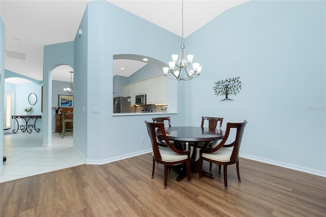 dining space with a notable chandelier, high vaulted ceiling, and light wood-type flooring