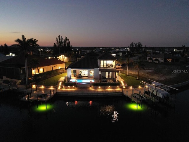 back house at dusk featuring a water view and a patio