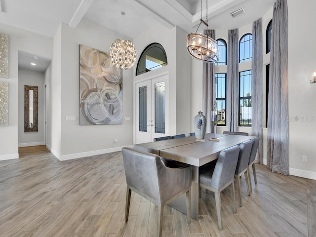 dining area with an inviting chandelier, a towering ceiling, light hardwood / wood-style flooring, and french doors