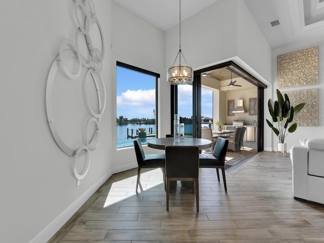 dining room with a water view, a chandelier, light hardwood / wood-style floors, and a high ceiling