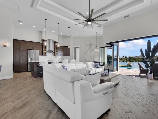 living room featuring a water view, a tray ceiling, ceiling fan, light hardwood / wood-style floors, and a high ceiling