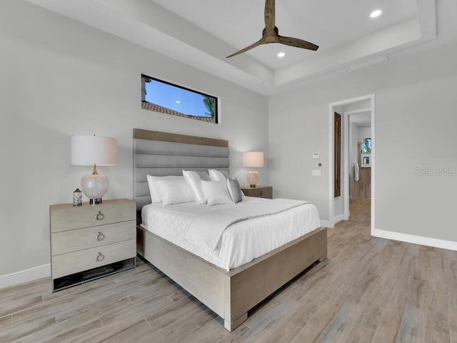 bedroom with a raised ceiling, ceiling fan, and light hardwood / wood-style flooring