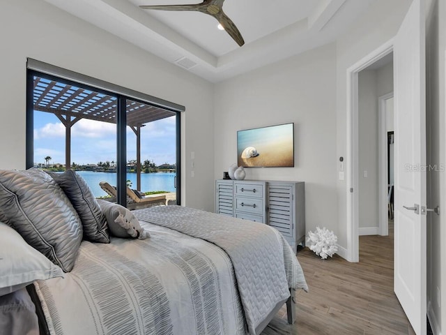 bedroom with ceiling fan, wood-type flooring, a tray ceiling, and access to outside