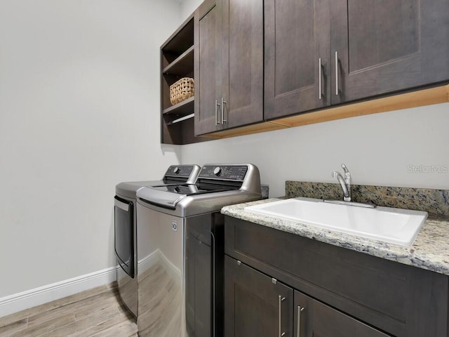 washroom featuring cabinets, sink, washing machine and clothes dryer, and light wood-type flooring