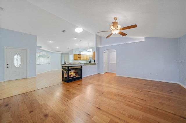 unfurnished living room with arched walkways, baseboards, lofted ceiling, ceiling fan, and light wood-style floors