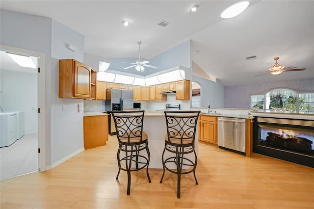 kitchen featuring a center island, stainless steel appliances, light countertops, a kitchen bar, and separate washer and dryer