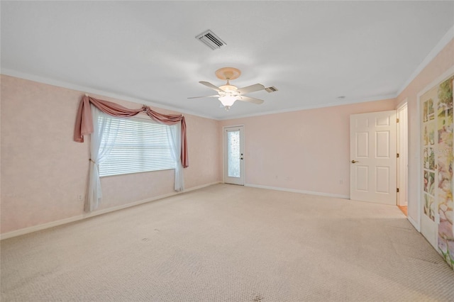 spare room with crown molding, light colored carpet, visible vents, a ceiling fan, and baseboards