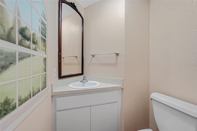 bathroom with a textured wall, vanity, and toilet