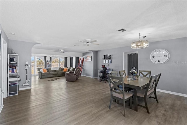 dining space featuring dark wood-type flooring, ceiling fan with notable chandelier, and a textured ceiling