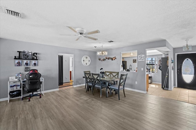 dining space featuring ceiling fan with notable chandelier, a textured ceiling, and light hardwood / wood-style floors