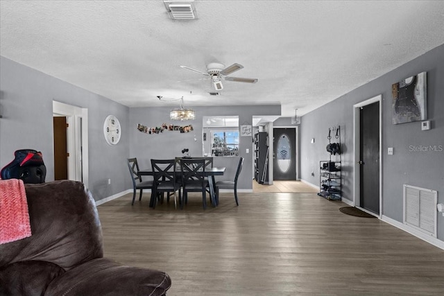 dining area with ceiling fan with notable chandelier, a textured ceiling, and dark hardwood / wood-style flooring