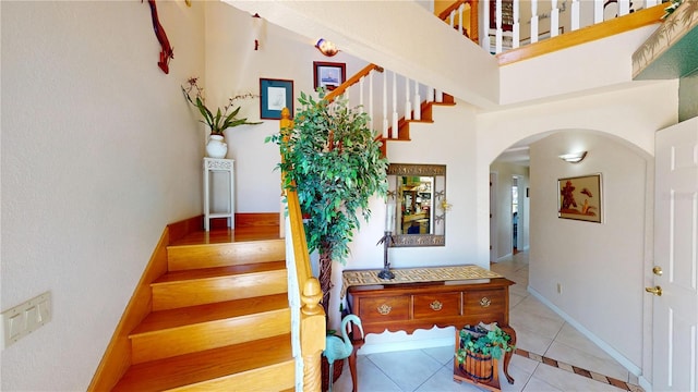 stairs featuring a towering ceiling, tile patterned flooring, arched walkways, and baseboards