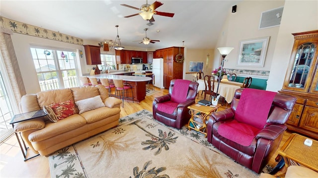 living room featuring light wood-type flooring, high vaulted ceiling, ceiling fan, and visible vents